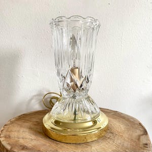 Puede incluir: Una lámpara de mesa vintage con una pantalla de cristal transparente acanalado y un patrón de diamantes decorativo. La base es de metal dorado pulido. La lámpara está diseñada para una sola bombilla.