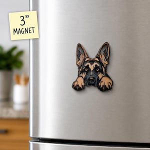 May include: A 3-inch magnet featuring a detailed illustration of a German Shepherd dog head with its front paws resting below its chin. The dog has black and tan fur, pointed ears, and dark eyes, displayed on a metallic refrigerator surface.