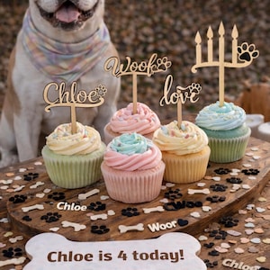 Peut inclure: Une fête d'anniversaire sur le thème des chiens avec des cupcakes avec un glaçage pastel et des décorations en bois avec les mots "Chloe", "Woof" et "love". Les cupcakes sont sur une planche en bois avec des empreintes de pattes et des os. Un chien est en arrière-plan.