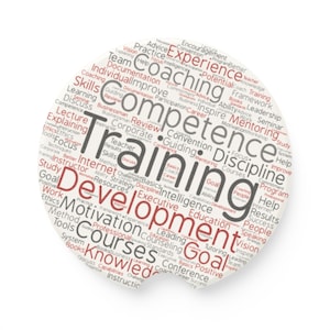 May include: A circular coaster featuring a word cloud design with various professional development terms in red and grey text. Prominent words include Training, Development, Competence, Coaching, and Mentoring, arranged in a dense, multi-directional layout.