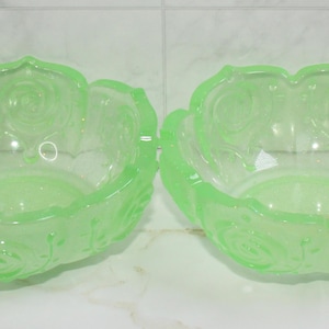 May include: Two light green glass bowls with a floral design. The bowls have a scalloped edge and a rose pattern. The bowls are made of a translucent glass material.