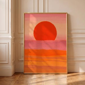 Könnte beinhalten: Ein rechteckiger Wandkunstdruck in einem dünnen goldenen Rahmen mit einem stilisierten Sonnenuntergang. Ein großer, roter Kreis befindet sich über einer Horizontlinie vor einem Hintergrund aus horizontalen Streifen in Rosa-, Orange- und Gelbtönen.