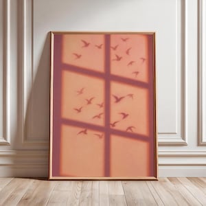 Könnte beinhalten: Ein rechteckiger gerahmter Wandkunstdruck mit einem weichen pfirsichfarbenen Hintergrund, überlagert vom dunklen, unscharfen Schatten eines Fenstersprossengitters und den Silhouetten zahlreicher kleiner Vögel, die in verschiedene Richtungen fliegen.