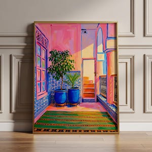 May include: A framed art print depicting a vibrant courtyard scene. The artwork features a pink and blue color palette, with potted plants, a green rug, and architectural details. The scene is bathed in sunlight, creating a warm and inviting atmosphere.