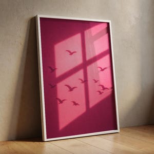 Könnte beinhalten: Ein vertikaler, rechteckiger Wandkunstdruck in einem weißen Rahmen mit einem tief magentafarbenen Hintergrund, auf dem der dunkle Schatten eines Fensterrahmens ein Kreuz in die Mitte wirft und Silhouetten mehrerer fliegender Vögel zu sehen sind.