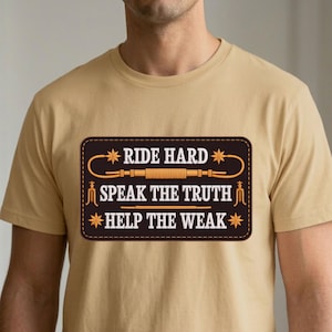 May include: A tan t-shirt featuring a rectangular patch with the text "RIDE HARD SPEAK THE TRUTH HELP THE WEAK". The patch has a dark brown border and a design of a rope and stars.