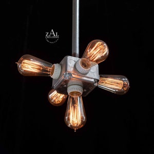 Może przedstawiać: Sześciopunktowa lampa wisząca z odsłoniętymi przewodami i żarówkami Edison. Lampa wykonana jest z metalu i ma srebrne wykończenie. Żarówki są ułożone w kształcie gwiazdy.
