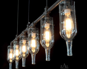 May include: A six-light industrial style chandelier made from repurposed wine bottles and black metal pipe. The chandelier has a rustic look and is perfect for a modern or farmhouse style home.