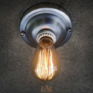 Puede incluir: Una lámpara de techo plateada con un casquillo de porcelana blanca y una bombilla incandescente de estilo vintage.