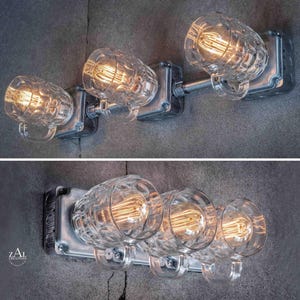 May include: A wall-mounted light fixture featuring three clear glass beer mug-shaped shades. Each shade houses a warm-toned Edison bulb. The fixture is mounted on a metallic base, creating an industrial aesthetic.
