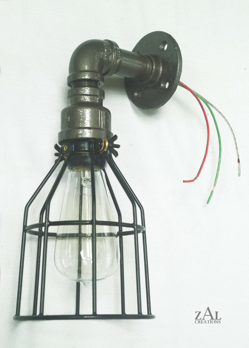 May include: A black metal cage light fixture with a clear glass bulb. The fixture is attached to a gray metal pipe and a round wall mount. The wires are visible and are red, green, and white.