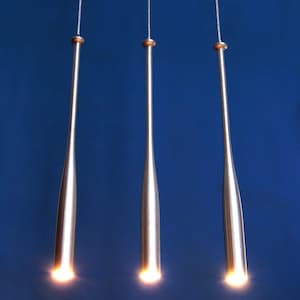 May include: Three silver pendant lights shaped like baseball bats hanging from the ceiling against a blue background. The lights are turned on and glowing.