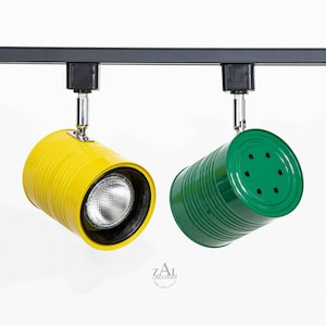 May include: Two track lighting fixtures made from repurposed tin cans. One is yellow and the other is green. Both have a black metal base and a clear glass light bulb.
