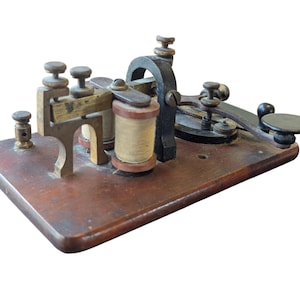 May include: Antique telegraph key on a wooden base. The key features brass and black metal components, including coils, levers, and knobs. The wooden base has a rich, dark brown color, showing signs of age and use. A vintage communication device.