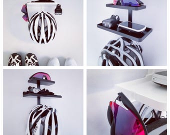 May include: A collection of cycling gear, including a white and black helmet, sunglasses, a bike light, and shoes. The items are displayed on a wall-mounted shelf system, showcasing a modern and organized approach to storage.