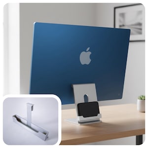 May include: A blue iMac computer with a silver stand, displaying the Apple logo. The stand has a built-in phone holder. An additional silver accessory is shown in the lower left corner. The computer is on a wooden desk.