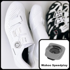 Op de afbeelding: Witte fietsschoenen met een BOA-draaisluitsysteem en een bandje. De schoenen hebben perforaties voor ventilatie. Een grijze en zwarte schoenplaat wordt getoond met de tekst "Wahoo Speedplay".