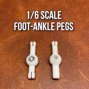 Puede incluir: Dos clavijas blancas de pie-tobillo a escala 1/6. Cada clavija tiene un cuerpo cilíndrico con una cabeza de tornillo y una base bifurcada. El texto "1/6 SCALE FOOT-ANKLE PEGS" se muestra en letras blancas sobre un fondo marrón.
