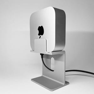 Könnte beinhalten: Ein silberner Computerturm mit schwarzem Apple-Logo ist auf einem silbernen Ständer montiert. Ein schwarzes Kabel führt vom Computer weg. Der Ständer hat eine rechteckige Basis und eine vertikale Halterung mit Aussparung.