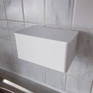 Può includere: Un contenitore rettangolare bianco montato su una parete piastrellata. Il contenitore ha un design semplice e minimalista con angoli arrotondati e una superficie liscia. Sembra vuoto e pronto per l'uso.