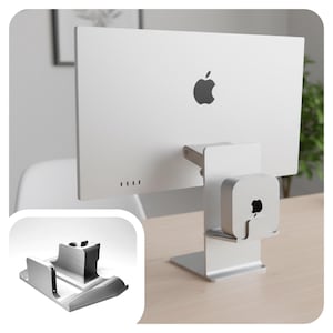May include: A silver metal computer monitor stand featuring an integrated mounting bracket on the back. The stand holds a small square silver computer device with an Apple logo. A separate view shows the empty silver metal stand from a front angle.