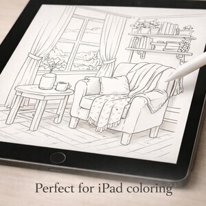 May include: An iPad displays a black and white line drawing of a cozy living room scene. The illustration includes a comfortable armchair with a blanket, a small side table with a cup and plant, and a window with curtains. A white stylus hovers over the drawing.