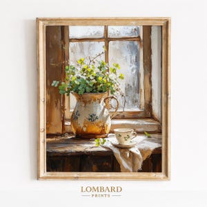 May include: A framed print of a still life scene. A rustic, yellow and blue floral pitcher holds green foliage. A teacup and saucer sit on a white cloth. The scene is set by a window with a view of the outside.
