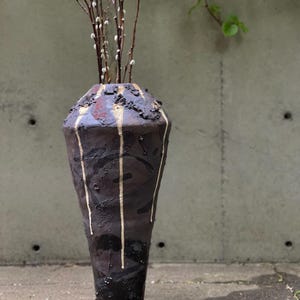 Könnte beinhalten: Eine hohe, dunkelbraune Keramikvase mit strukturierter Oberfläche und goldenen Akzenten. Die Vase hat eine einzigartige, geometrische Form und ist mit mehreren Zweigen von Kätzchenweiden gefüllt. Die Vase ist etwa 61 cm hoch.