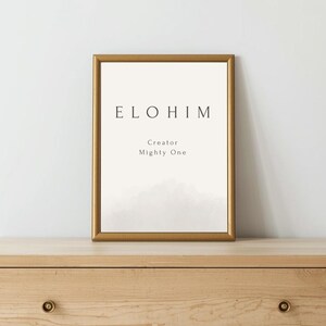 Puede incluir: Una impresión enmarcada con la palabra "ELOHIM" en letras mayúsculas negras. Debajo, las palabras "Creator" y "Mighty One" están impresas. El marco es dorado y el fondo es de color crema claro. La impresión se muestra en una cómoda de madera.
