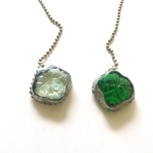 May include: Two decorative leaf-shaped ceiling fan pulls. One is clear with iridescent accents, the other is green. Both are encased in a silver-colored metal frame and attached to a silver beaded chain.
