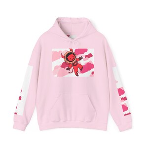 May include: A light pink hoodie with a front pocket and a hood. The front features a cartoon illustration of a red devil in a spacesuit floating among pink clouds. The sleeves have a white stripe with pink cloud graphics.