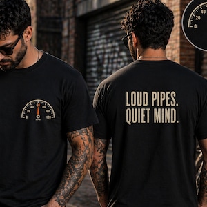 Op de afbeelding: Zwart T-shirt met een snelheidsmeter op de voorkant en de tekst "LOUD PIPES. QUIET MIND." op de achterkant. De snelheidsmeter geeft 60 mph (97 km/h) aan. Het shirt heeft korte mouwen en een ronde hals.