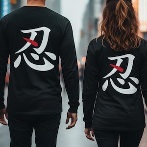 May include: Two black long-sleeve shirts featuring a large white Japanese kanji character on the back with a small red horizontal dash accent. The shirts are worn with black trousers, showcasing a matching design on the back of each garment.