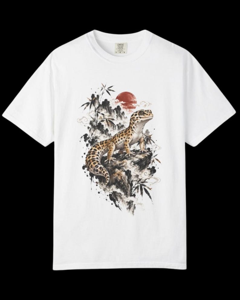 Może przedstawiać: Biały t-shirt z kr&oacute;tkim rękawem z nadrukiem graficznym przedstawiającym cętkowanego gekona lamparciego siedzącego na skale. Wz&oacute;r zawiera czarne pociągnięcia pędzla, łodygi bambusa i czerwone koło słońca w tle, tworząc szczeg&oacute;łową kompozycję.