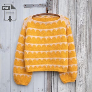 May include: A yellow sweater with white scalloped patterns. The sweater has long sleeves and a round neckline. The garment is hanging on a wooden hanger against a weathered wood background. The sweater is a cozy knit.