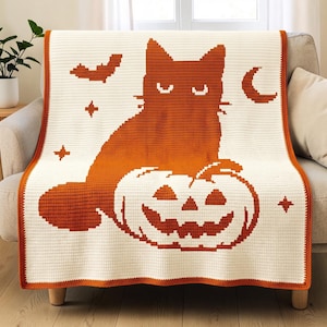 May include: A cream-colored crochet blanket featuring a large orange cat sitting behind a carved jack-o'-lantern pumpkin. The design includes orange silhouettes of a bat, a crescent moon, and several four-pointed stars, finished with an orange border.