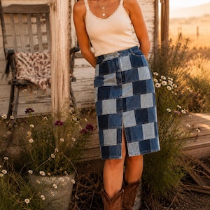 Puede incluir: Una mujer con una camiseta sin mangas color crema con ribete de encaje y una falda vaquera patchwork. También lleva botas de vaquero marrones. El fondo incluye un porche de madera, una mecedora y flores silvestres.