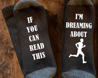 May include: A pair of dark grey socks with white text and a graphic. The left sock reads IF YOU CAN READ THIS and the right sock reads I'M DREAMING ABOUT with a white silhouette of a person running. The socks have ribbed cuffs.