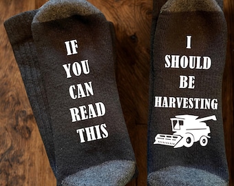 May include: A pair of dark grey socks with contrasting light grey heels and toes. The left sock features the white text IF YOU CAN READ THIS, and the right sock features the white text I SHOULD BE HARVESTING above a white combine harvester icon.
