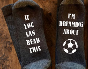 May include: A pair of dark grey socks with white text and a football graphic. The left sock features the text IF YOU CAN READ THIS, and the right sock features the text I'M DREAMING ABOUT above a graphic of a black and white football.