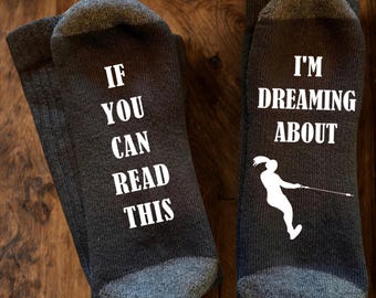 May include: A pair of dark grey socks with white text and a graphic. The left sock reads IF YOU CAN READ THIS and the right sock reads I'M DREAMING ABOUT with a white silhouette of a person wakeboarding on the water.