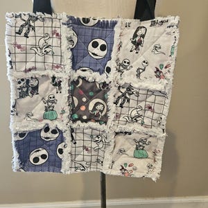 May include: A quilted tote bag featuring a patchwork design with frayed white edges. The fabric displays various character prints from The Nightmare Before Christmas, including Jack Skellington and Sally, in shades of black, white, grey, and teal.