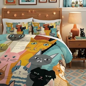 May include: A bedding set featuring a colourful, repeating pattern of various cat faces in shades of orange, pink, blue, grey, and black. The comforter and matching pillow shams display stylised feline illustrations with distinct expressions.