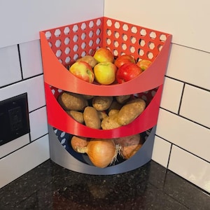 May include: A three-tiered, corner-shaped storage bin in red, gray, and blue, filled with apples, potatoes, and onions. The top section is red with a honeycomb pattern, the middle is red, and the bottom is gray.