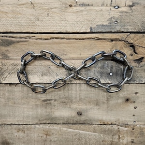 May include: A metal chain shaped into an infinity symbol, set against a backdrop of weathered wooden planks. The chain links are a dark, metallic gray, creating a contrast with the light brown wood. The wood has visible grain and nail heads.