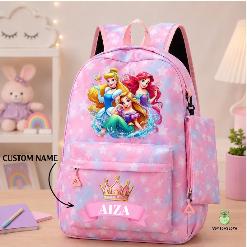 K&ouml;nnte beinhalten: Ein rosa-blauer Tie-Dye-Rucksack mit Sternenmuster und einer Grafik von drei Prinzessinnen. Die Vordertasche zeigt eine goldene Krone &uuml;ber einem rosa Banner mit dem Namen AIZA in Wei&szlig;. Ein passendes Federm&auml;ppchen ist an der Seite befestigt.