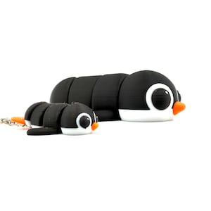 May include: Two black and white penguin-shaped figurines with orange beaks. One is larger and segmented, resembling a caterpillar. The smaller one is attached to a keychain. Both have large, round eyes.
