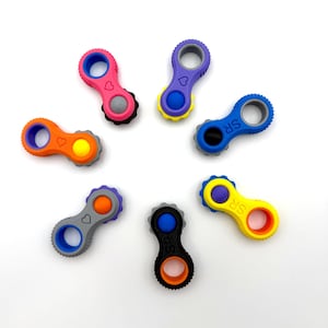 Könnte beinhalten: Eine Sammlung farbenfroher, kettenförmiger Zappelspielzeuge. Jedes Spielzeug hat an jedem Ende eine kreisförmige Öffnung, die durch einen Mittelteil mit einem Herz- oder Kreisdesign verbunden ist. Farben sind Pink, Lila, Orange, Blau, Gelb, Grau und Schwarz.