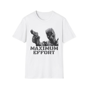 Könnte beinhalten: Weißes T-Shirt mit einer Schwarz-Weiß-Grafik eines maskierten Charakters, der eine Waffe hält. Der Text "MAXIMUM EFFORT" ist in grauen Buchstaben darunter gedruckt. Das T-Shirt hat einen Rundhalsausschnitt und kurze Ärmel.
