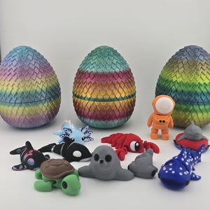 May include: An assortment of colorful, dragon-scale patterned egg-shaped containers, each approximately 4 inches tall, with various small animal figurines, including a turtle, seal, and whale. An astronaut figure is also present.
